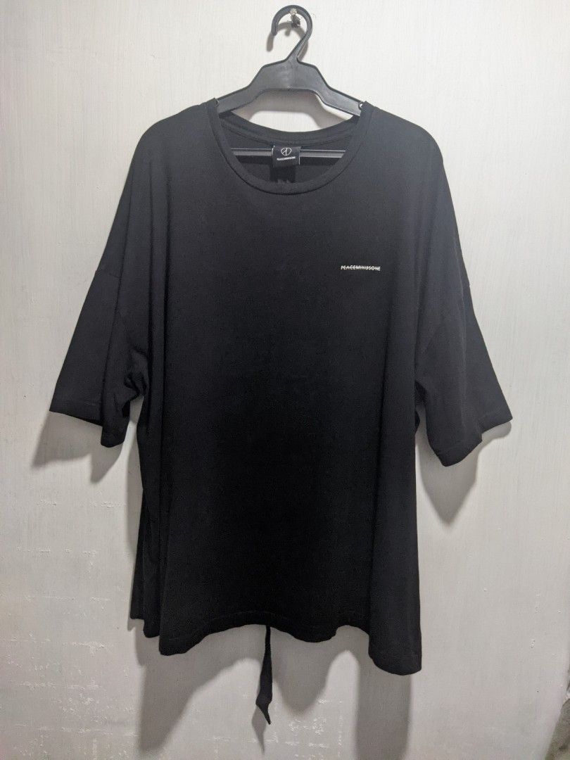 PEACEMINUSONE Black Oversized T-shirt (Category: Tshirts & Polo Shirts ) located in Dasmarinas. Submitted by _thrift.lang_ (Listing ID 1425370190, Image 1). Description: Black oversized t-shirt from PEACEMINUSONE. Features a small white logo on the front and the brand's logo on the neck label. The back of the neck label has a printed quote. The shirt has a unique design with a tie detail at the bottom..
