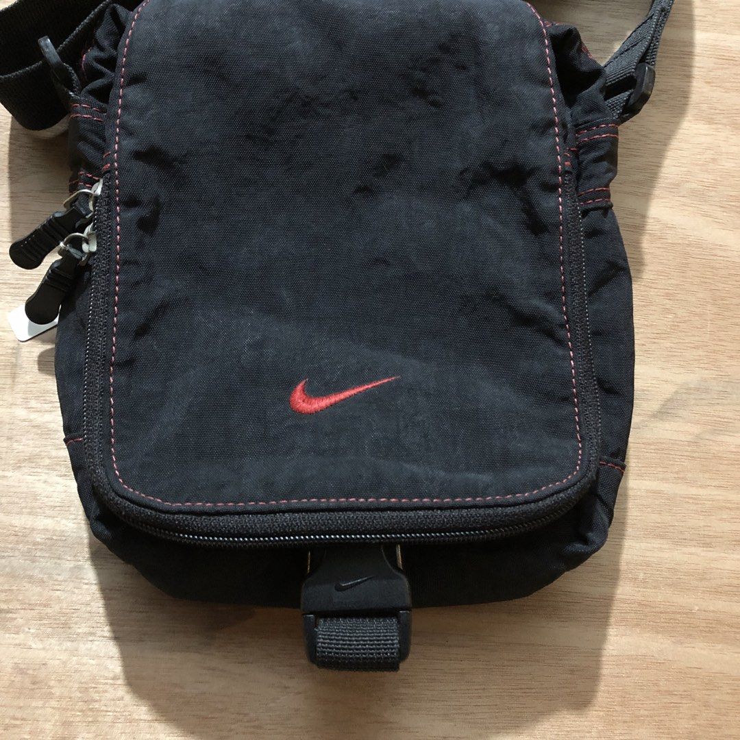 VINTAGE Nike Small Shoulder Bag Black (Category: Sling Bags) located in Davao. Submitted by repurposekultyurph (Listing ID 1425277242, Image 3). Description: Black VINTAGE Nike shoulder bag with a red swoosh logo. Features a main compartment, a front pocket, and an adjustable shoulder strap. The bag has red stitching details and a Nike branded buckle. Made in Korea. EXCELLENT CONDITION NO MAJOR ISSUES READY TO WEAR .