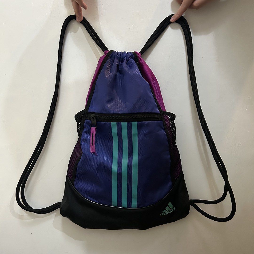 Adidas Drawstring Bag with Front Pocket (Category: Backpacks) located in Baguio. Submitted by rmlst.coll (Listing ID 1425536636, Image 1). Description: Adidas drawstring bag in purple, teal, and black. Features a front zippered pocket and a mesh side pocket. The bag has the Adidas logo on the bottom. The drawstring closure is black. The bag is designed with three teal stripes down the front..
