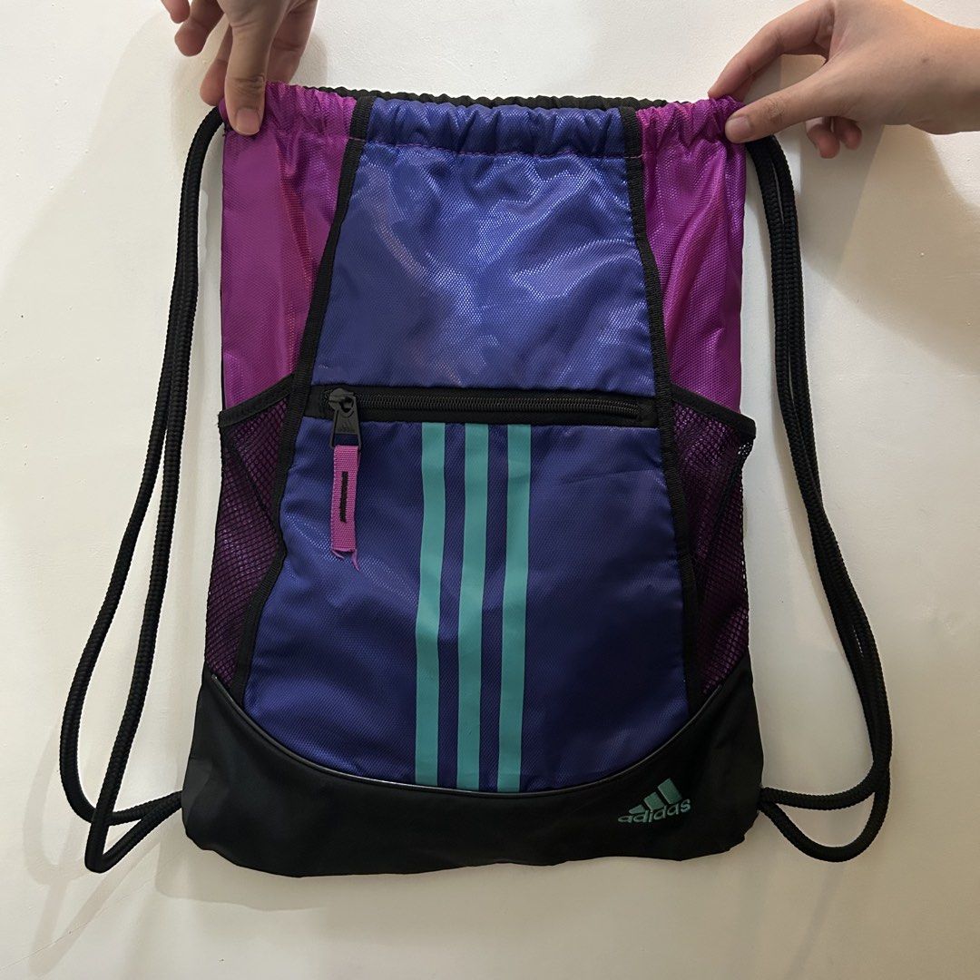 Adidas Drawstring Bag with Front Pocket (Category: Backpacks) located in Baguio. Submitted by rmlst.coll (Listing ID 1425536636, Image 3). Description: Adidas drawstring bag in purple, teal, and black. Features a front zippered pocket and a mesh side pocket. The bag has the Adidas logo on the bottom. The drawstring closure is black. The bag is designed with three teal stripes down the front..