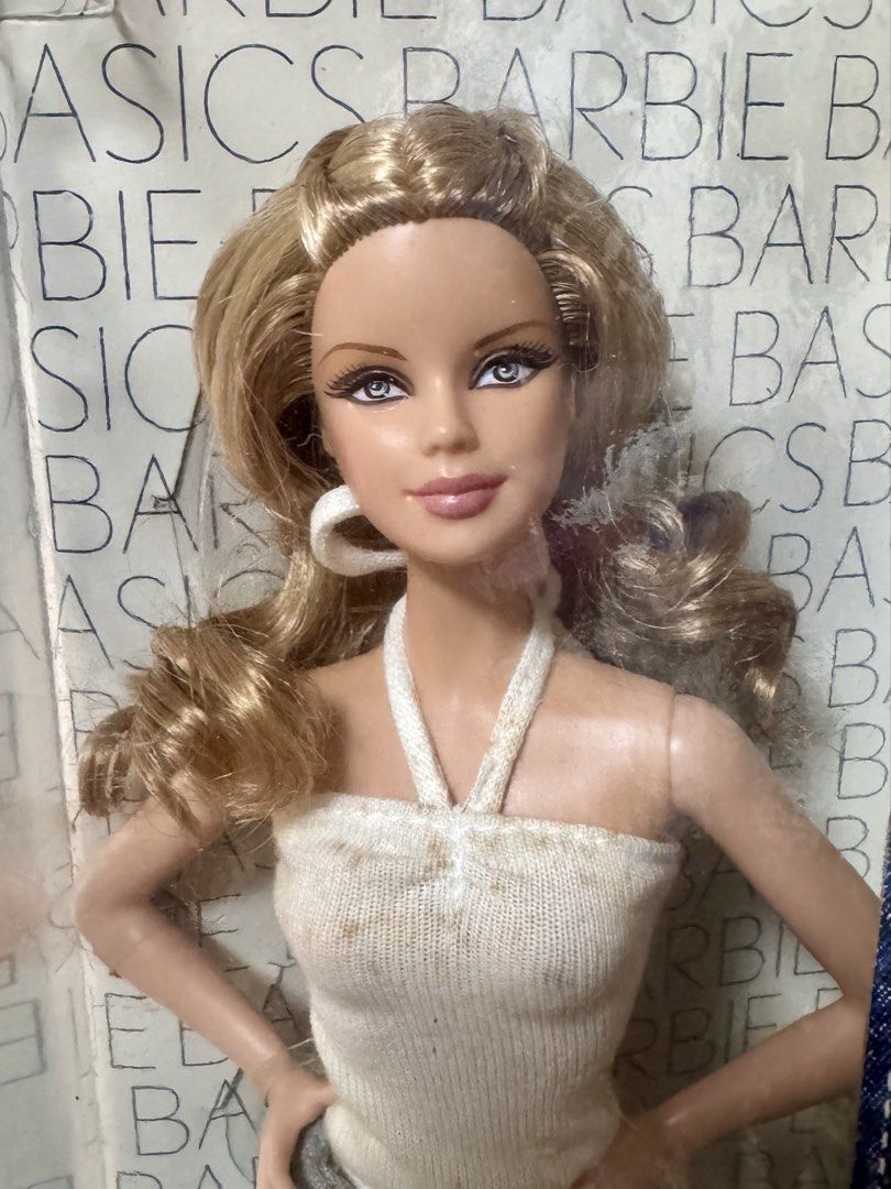 Barbie Basics Jeans Mackie Doll NRFB (Category: Kids Toys) located in Pasig City. Submitted by rcdc526 (Listing ID 1425496062, Image 3). Description: Barbie Basics Jeans Mackie doll features a blonde hairstyle and is wearing a white halter top and blue jeans. The doll has hoop earrings and is in its original packaging. The box has a barcode sticker on it. The doll is part of the Black Label collection. Taking Offers + Shipping Fee PM me if intere