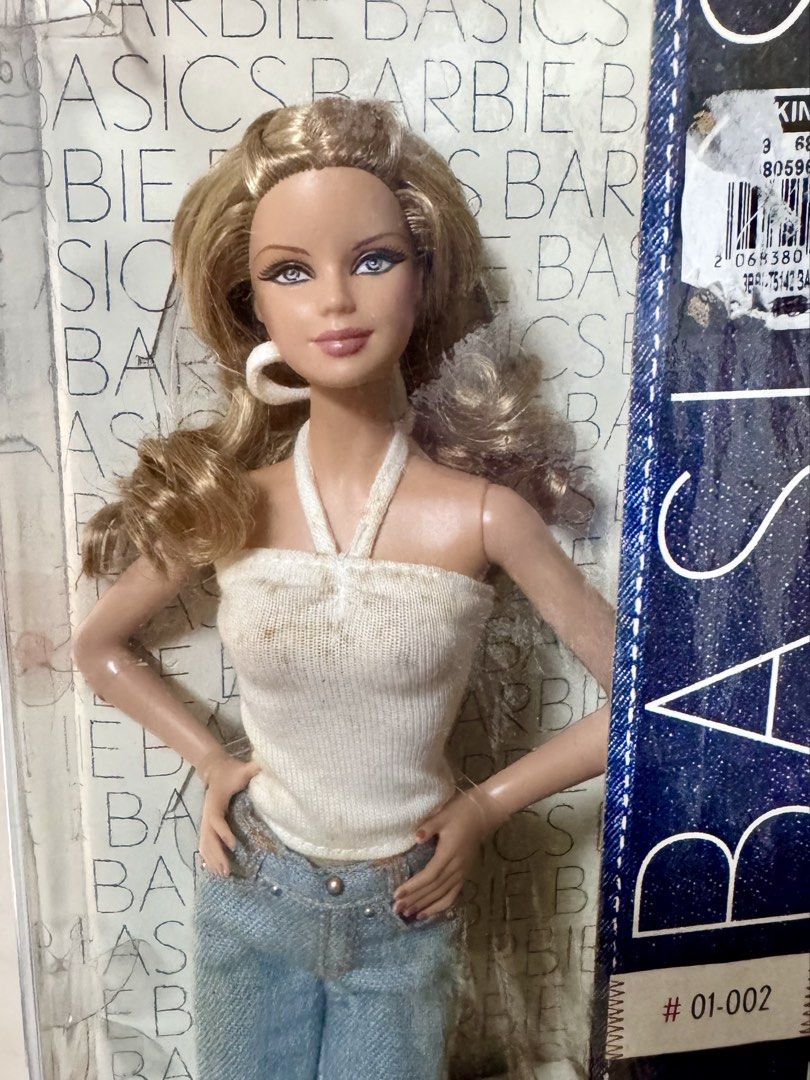 Barbie Basics Jeans Mackie Doll NRFB (Category: Kids Toys) located in Pasig City. Submitted by rcdc526 (Listing ID 1425496062, Image 2). Description: Barbie Basics Jeans Mackie doll features a blonde hairstyle and is wearing a white halter top and blue jeans. The doll has hoop earrings and is in its original packaging. The box has a barcode sticker on it. The doll is part of the Black Label collection. Taking Offers + Shipping Fee PM me if intere