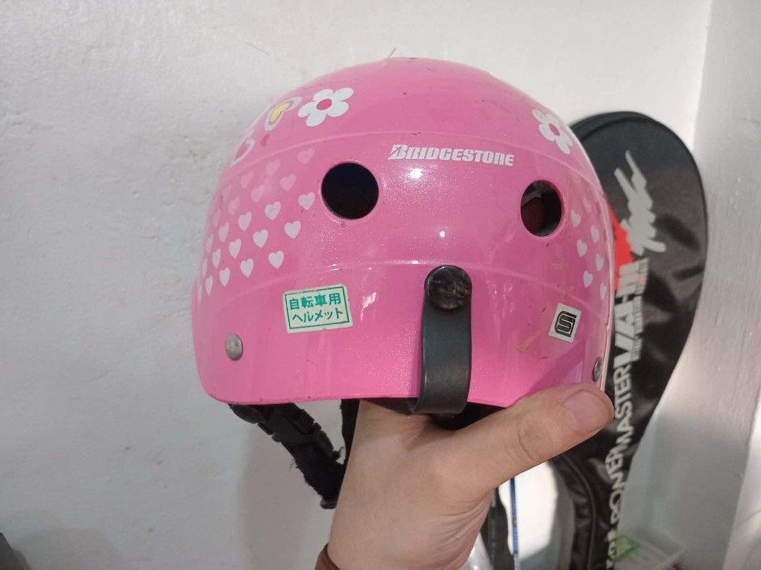 Bridgestone Pink Helmet (Category: Bicycles) located in Taguig. Submitted by ashicollection (Listing ID 1425602027, Image 2). Description: Pink helmet with a visor. Features floral and heart designs. Includes a chin strap for secure fit. The interior has padding for comfort and protection. The helmet has several ventilation holes. The brand name "Bridgestone" is visible on the helmet..
