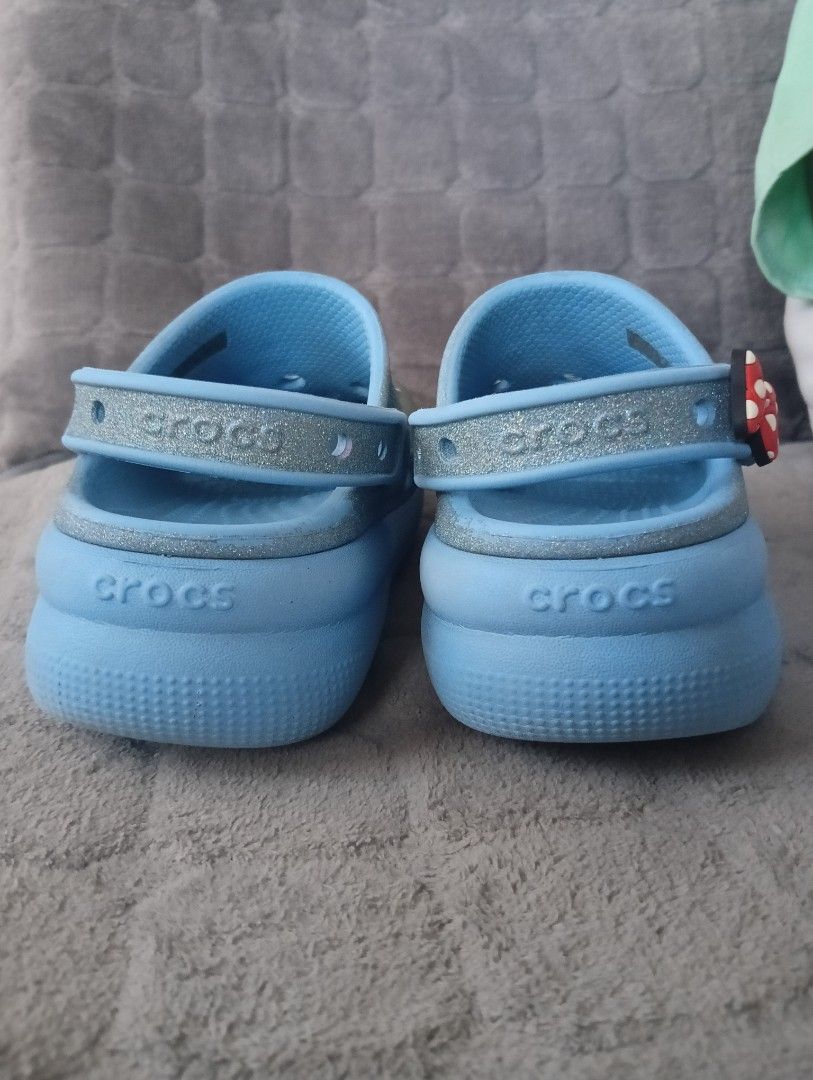 Crocs Frozen Jibbitz Clogs (Category: Babies & Kids Fashion) located in Santa Rosa. Submitted by amiraamara (Listing ID 1425499087, Image 3). Description: Light blue Crocs clogs with Frozen-themed Jibbitz. Features a glittery finish and a raised sole. Includes Jibbitz of Olaf, Elsa, and other Frozen characters. The size is J1. The Crocs logo is visible on the side and sole of the shoes. The heel strap has the Crocs logo..