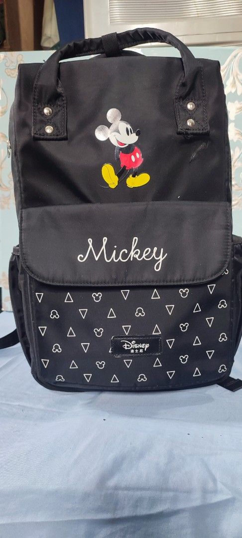 Disney Mickey Mouse Diaper Bag (Category: Diaper Bags & Wetbags) located in Manila. Submitted by mhitchz10 (Listing ID 1425519538, Image 2). Description: Black diaper bag featuring a Mickey Mouse design. It has a front flap with the word "Mickey" embroidered on it. The bag has multiple compartments, including side pockets and a spacious interior. It also has adjustable straps and a top handle for easy carrying. Dimensions are approximately L-16, 