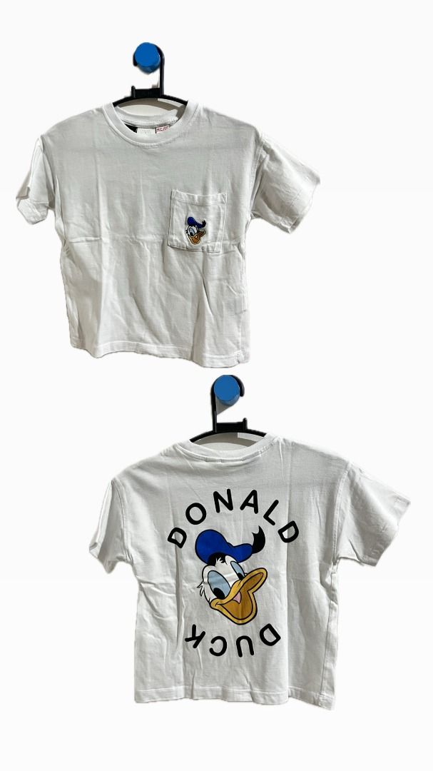 Donald Duck White T-shirt (Category: Babies & Kids Fashion) located in Villasis. Submitted by evangelist79838 (Listing ID 1425490976, Image 1). Description: White t-shirt featuring a Donald Duck design. The front has a small pocket with a Donald Duck graphic. The back of the shirt displays a larger Donald Duck graphic with the words "DONALD DUCK" above and below the character. The shirt has short sleeves and a crew neck..