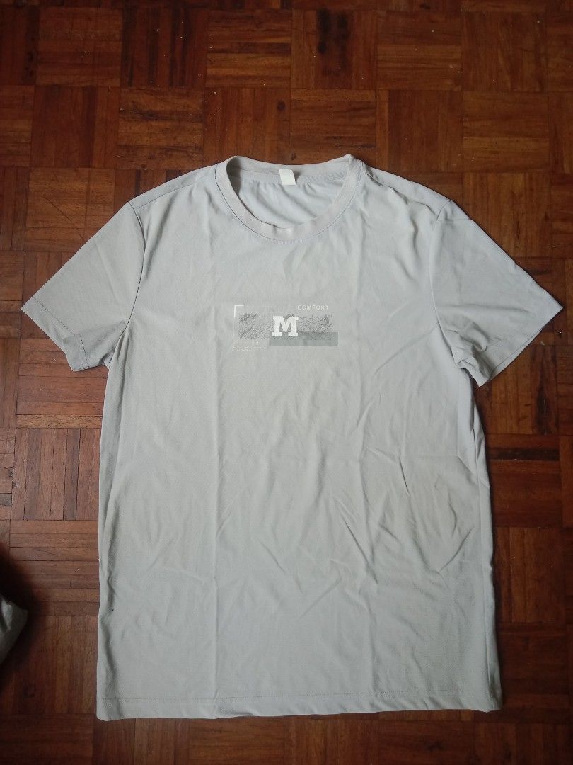 Gray T-shirt with Logo -M-L Size (Category: Tshirts & Polo Shirts ) located in Marikina City. Submitted by cathdeeee (Listing ID 1425560716, Image 1). Description: Gray t-shirt with a logo on the front. It has short sleeves and a crew neck. The shirt is laid flat on a wooden surface..