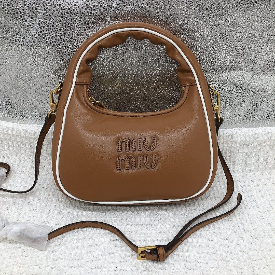 Miu Miu Leather Hobo Bag (Category: Luxury Bags & Wallets) located in Bocaue. Submitted by bagsbyjayce (Listing ID 1425475540, Image 1). Description: Miu Miu handbag features a brown leather exterior with a white trim. It has a top handle and a detachable shoulder strap. The bag has a zipper closure and a gold-tone hardware. The interior is lined with a satin-like fabric. The Miu Miu logo is embossed on the front of the bag..