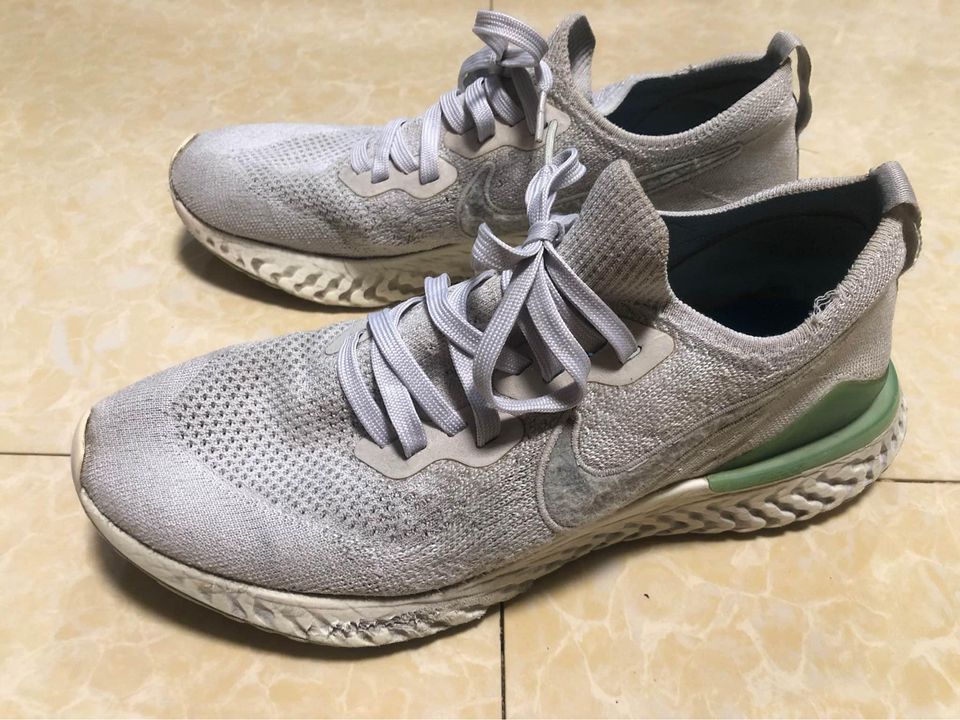 Nike Epic React Flyknit 2 'Vast Grey Blue Lagoon' US9 (Category: Sneakers) located in Mandaluyong City. Submitted by alexis_77 (Listing ID 1425492657, Image 3). Description: Nike Epic React Flyknit running shoes in a light grey color. Features a knit upper, lace-up closure, and a React foam midsole. The shoes have a green accent on the heel and a white sole. The Nike swoosh logo is visible on the side of the shoe. Stocked and stored. Buy at your 