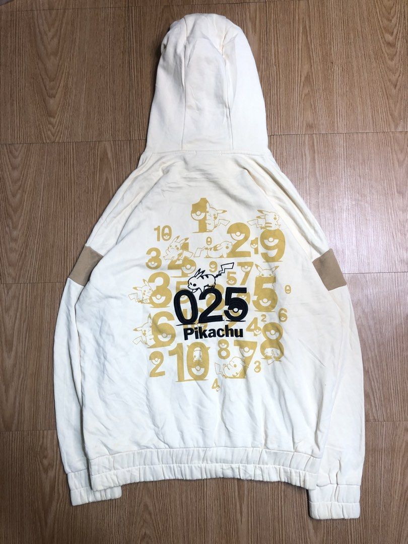 Pikachu Hoodie (Category: Hoodies) located in Quezon City. Submitted by yeahsource222 (Listing ID 1425623312, Image 2). Description: Cream-colored hoodie featuring a Pikachu design on the front and back. The front has a Pikachu graphic and a kangaroo pocket. The back displays the number "025" with Pikachu illustrations and other numbers. It has a drawstring hood and ribbed cuffs and hem. The sleeves have brown patches..