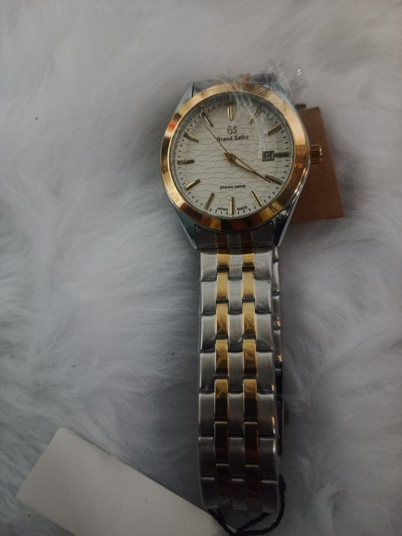 Seiko Grand Seiko Watch (Category: Luxury Watches) located in Manila. Submitted by crustynico23 (Listing ID 1425492468, Image 2). Description: Seiko Grand Seiko watch features a silver and gold-tone stainless steel band and a white dial. It has a date display and an automatic movement visible through the transparent case back. The watch includes a Seiko tag. The band has a two-tone design, with silver and gold links..