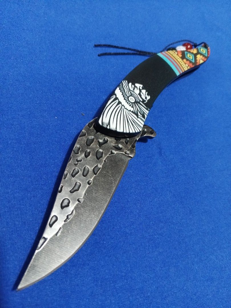 E.D.C - 08 (Category: Knives & Chopping Boards) located in Bulacan. Submitted by Sina_Unang_Yaman (Listing ID 1429504575, Image 2). Description: Pocket knife features a unique Native American design. The blade has a textured finish. The handle is black with colorful geometric patterns and a Native American chief illustration. It includes a lanyard with decorative beads and comes with a black box..