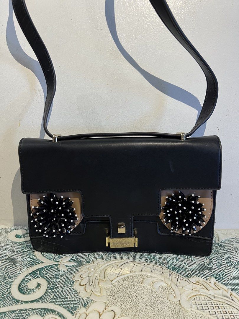 Hush Puppies Black Shoulder Bag (Category: Shoulder Bags) located in Makati City. Submitted by nicolaylay (Listing ID 1429504272, Image 1). Description: Black Hush Puppies shoulder bag with a flap closure. Features decorative embellishments on the front. Includes a top handle and a long shoulder strap. The bag has a gold-tone clasp and hardware. The back of the bag shows some wear. Flaw: See 3rd pic .