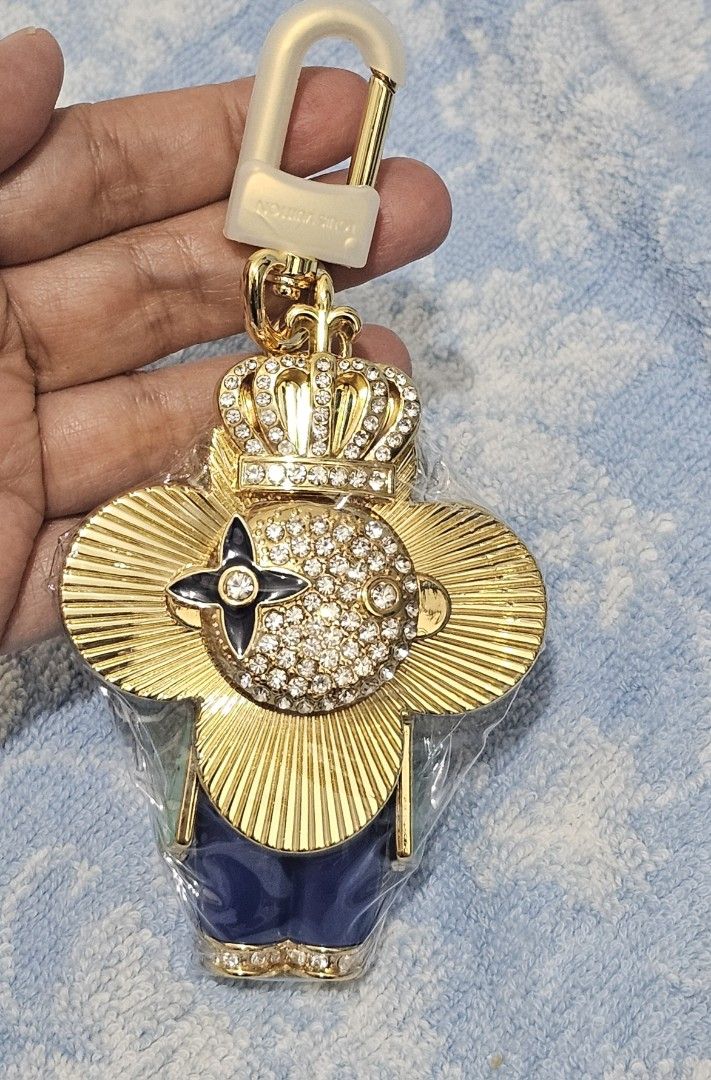 Louis Vuitton Crown Keychain (Category: Luxury Accessories) located in Quezon City. Submitted by lacygirlshoppe (Listing ID 1429617563, Image 1). Description: Louis Vuitton keychain features a gold-tone design with a crown and a flower emblem. It is adorned with sparkling crystals and has a blue base. Comes with box and Dust bag. The keychain includes a clasp for easy attachment..