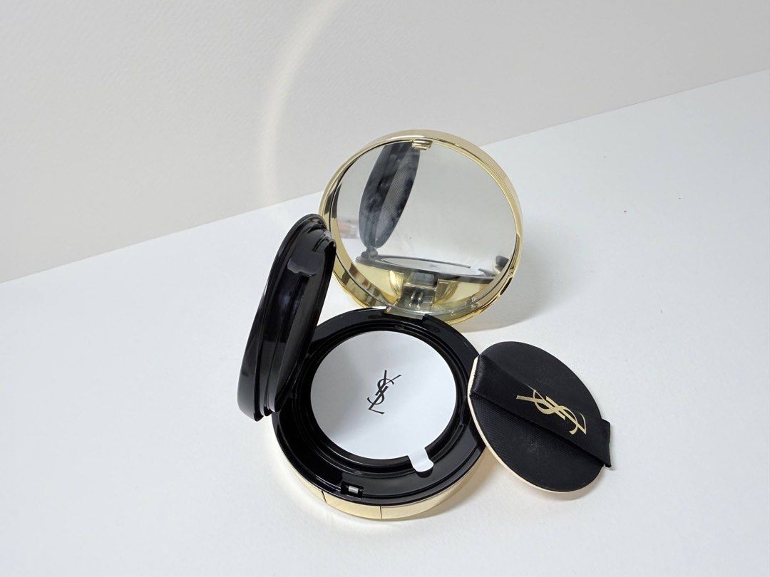 YSL Le Cushion Encre De Peau Foundation (Category: Makeup) located in Mandaluyong City. Submitted by lgariba (Listing ID 1429611042, Image 2). Description: YSL Le Cushion Encre De Peau Foundation. Includes the compact, mirror, and applicator puff. The shade is 30. The compact has a gold rim and a black top with the YSL logo. The back of the compact has product information. The foundation is a cushion type. Note: No more box.