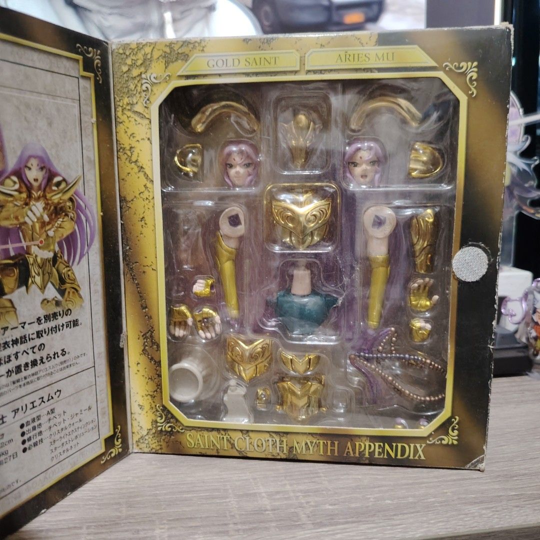 Bandai Saint Cloth Myth Appendix Aries Mu (Category: Figurines & Statues) located in Bulacan. Submitted by qilyuartstudio (Listing ID 1431276714, Image 2). Description: Bandai Saint Cloth Myth Appendix Aries Mu action figure. The box contains various parts, including armor pieces, multiple face options, and other accessories. The figure features a gold saint design. The box has Japanese text and the Bandai logo..