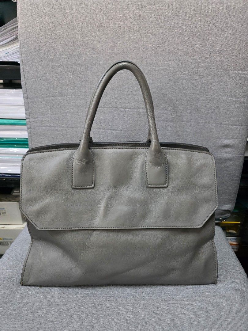 Prada Grey Leather Tote Bag (Category: Luxury Bags & Wallets) located in General Trias. Submitted by roselle2230 (Listing ID 1431272322, Image 2). Description: Prada tote bag features a sleek grey leather exterior. It has a top handle and a flap closure with a lock. The interior includes a zippered pocket and a Prada logo. The bag also has a triangular Prada logo on the exterior. Original leather material with key and platted logo.