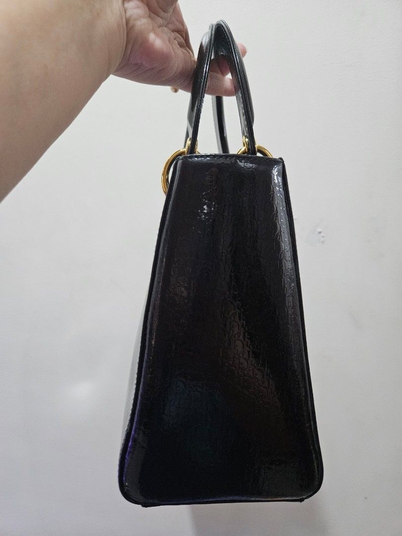 Lady Dior Black Patent Leather Handbag, Medium (Category: Luxury Bags & Wallets) located in Makati City. Submitted by ashasluxurycloset (Listing ID 1431449582, Image 3). Description: Elegant Dior black Diorissimo Lady Dior patent leather handbag. Features gold-tone hardware, including the iconic Dior charm and rings. The bag has a structured shape with a top handle and a zip closure. Includes protective feet on the bottom. 100% Guaranteed Authent