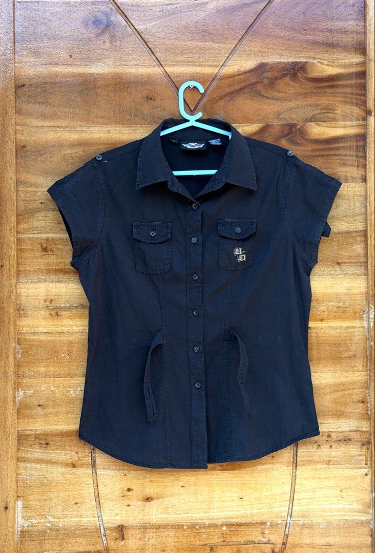 Harley-Davidson Black Short Sleeve Shirt (Category: Blouses) located in Cavite. Submitted by peppermintsss (Listing ID 1431440889, Image 1). Description: - Harley-Davidson black short sleeve shirt - Size: Medium - Features: - Button-down front - Two chest pockets - Tie detail at waist - Embroidered Harley-Davidson logo (front and back) - Material: Cotton ‼️bust: 38” ‼️Length: 24.5” 🛵 SF will be shouldered by the buyer.