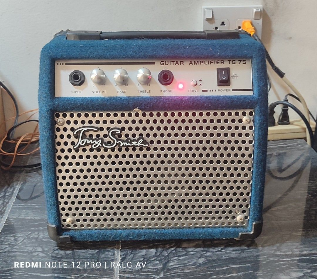 Tony Smith TG-75 Guitar Amplifier (Category: Musical Instruments) located in Bulacan. Submitted by ronald277077025 (Listing ID 1431468212, Image 1). Description: - Tony Smith TG-75 guitar amplifier - Controls: Input, Volume, Bass, Treble, Phone - Power switch and indicator light - Stylish blue fabric exterior - Metal speaker grill with Tony Smith logo - Includes caution label and power specifications on the back -110 volts.