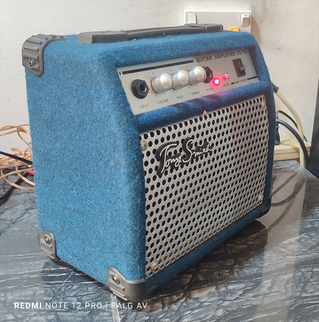 Tony Smith TG-75 Guitar Amplifier (Category: Musical Instruments) located in Bulacan. Submitted by ronald277077025 (Listing ID 1431468212, Image 2). Description: - Tony Smith TG-75 guitar amplifier - Controls: Input, Volume, Bass, Treble, Phone - Power switch and indicator light - Stylish blue fabric exterior - Metal speaker grill with Tony Smith logo - Includes caution label and power specifications on the back -110 volts.
