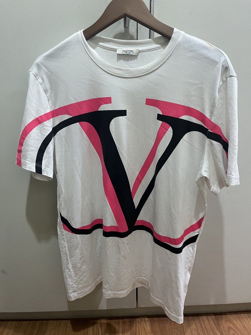 Valentino V-Logo T-Shirt (Category: Tshirts & Polo Shirts ) located in Manila. Submitted by wanwangaragesale (Listing ID 1431531767, Image 1). Description: - Authentic Valentino T-shirt - Features a bold V-logo in pink and black - Color: White - Neckline: Crew neck - Size: 50 - Material: Cotton and elastane blend - Made in China - Includes care instructions and brand tags.
