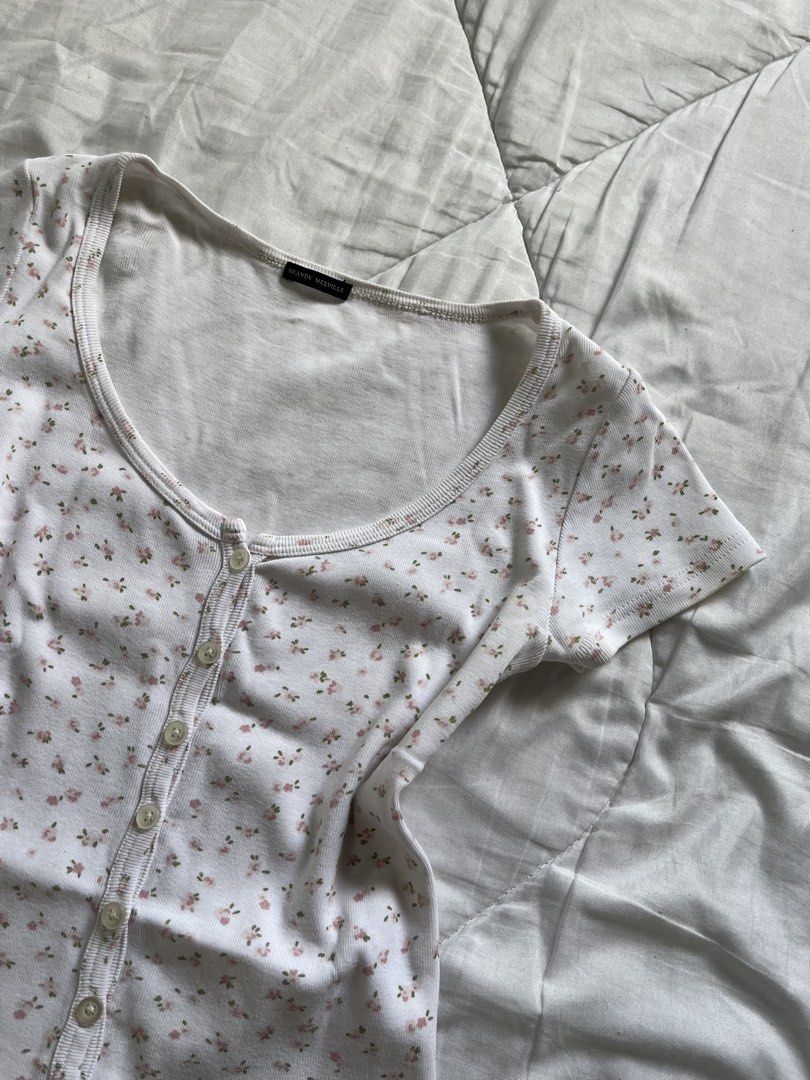 Brandy Melville Floral Baby Tee (Category: Sleeveless) located in Cavite. Submitted by siyaara (Listing ID 1431606049, Image 3). Description: - White top with floral pattern - Size: 15 - Features a scoop neckline - Short sleeves - Button-up front - Material: Cotton .