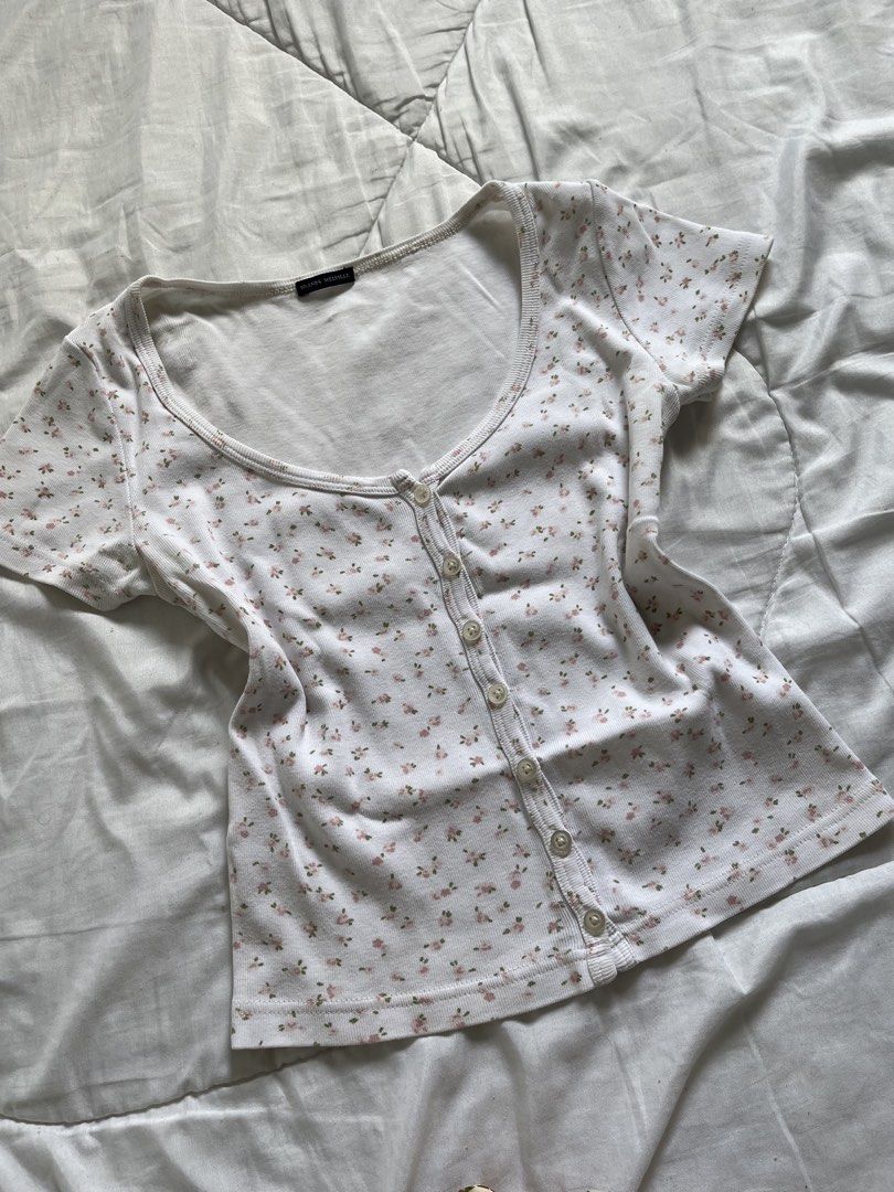 Brandy Melville Floral Baby Tee (Category: Sleeveless) located in Cavite. Submitted by siyaara (Listing ID 1431606049, Image 1). Description: - White top with floral pattern - Size: 15 - Features a scoop neckline - Short sleeves - Button-up front - Material: Cotton .