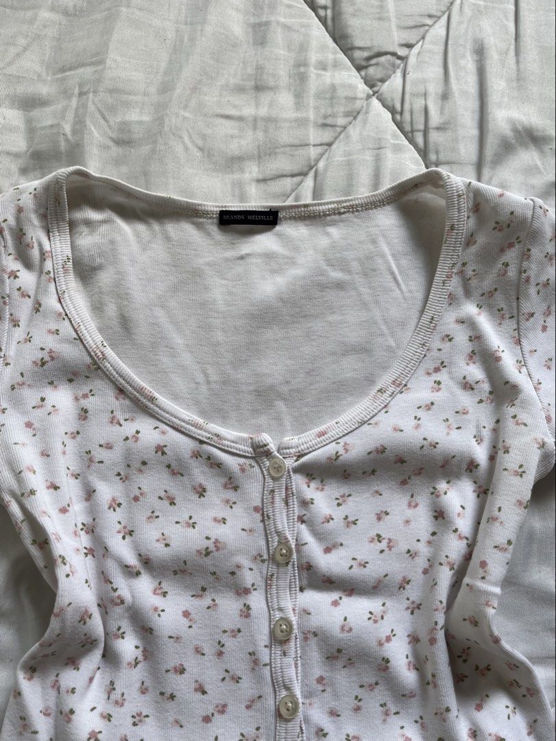 Brandy Melville Floral Baby Tee (Category: Sleeveless) located in Cavite. Submitted by siyaara (Listing ID 1431606049, Image 2). Description: - White top with floral pattern - Size: 15 - Features a scoop neckline - Short sleeves - Button-up front - Material: Cotton .