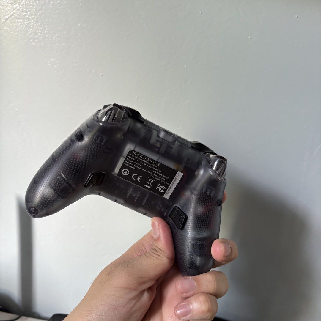 Machenike G3 V2 Tri-Mode Gaming Controller (Category: Controllers) located in Lala. Submitted by thirdeclutter (Listing ID 1431573045, Image 3). Description: Machenike G3 V2 controller. It comes with a charging dock. The controller has a transparent back. It features a standard button layout with a D-pad, two analog sticks, and action buttons. The controller has a USB-C port for charging. RFS: I don't need it anymore.