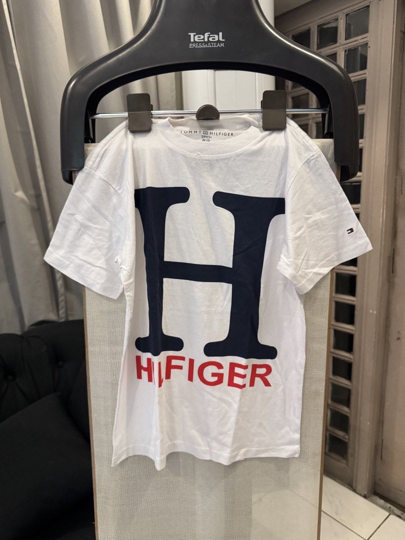 Tommy Hilfiger Graphic Tee (White, Size M) (Category: Blouses) located in Pasig City. Submitted by drea3600 (Listing ID 1431893298, Image 1). Description: Brand: Authentic Tommy Hilfiger Design: Large navy “H” with vertical red “HILFIGER” print Style: Classic crew neck T-shirt Size: Medium (M) Material: 100% Cotton – soft & breathable Origin: [Insert from tag if available, e.g., Made in Vietnam] Condition: Brand new (overrun / surplus) Fit: Men’s