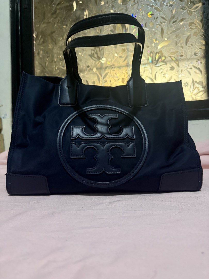 Tory Burch Ella Tote Bag (Category: Luxury Bags & Wallets) located in Pasig City. Submitted by help.a.hoarder.out (Listing ID 1431996814, Image 2). Description: - Tory Burch Ella tote bag - Color: Navy blue - Features embossed logo - Leather handles - Magnetic fastening - Spacious interior - Zippered pocket - Shows wear on corners and needs repainting - Worn out due to daily use at school - Negotiable.