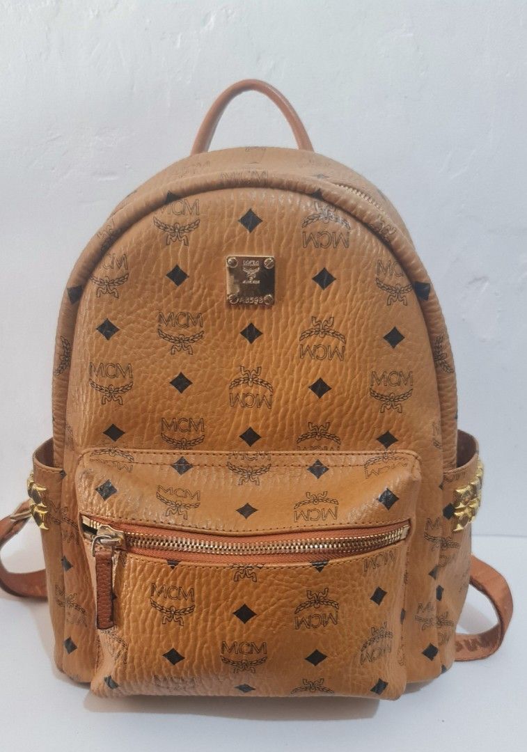 Authentic MCM Backpack (Category: Luxury Bags & Wallets) located in Lucena. Submitted by gwenbibi17 (Listing ID 1428993436, Image 2). Description: Brown MCM backpack with a front zippered pocket. Features the MCM logo pattern and a small metal logo plate. The backpack has gold-colored hardware and studded accents..
