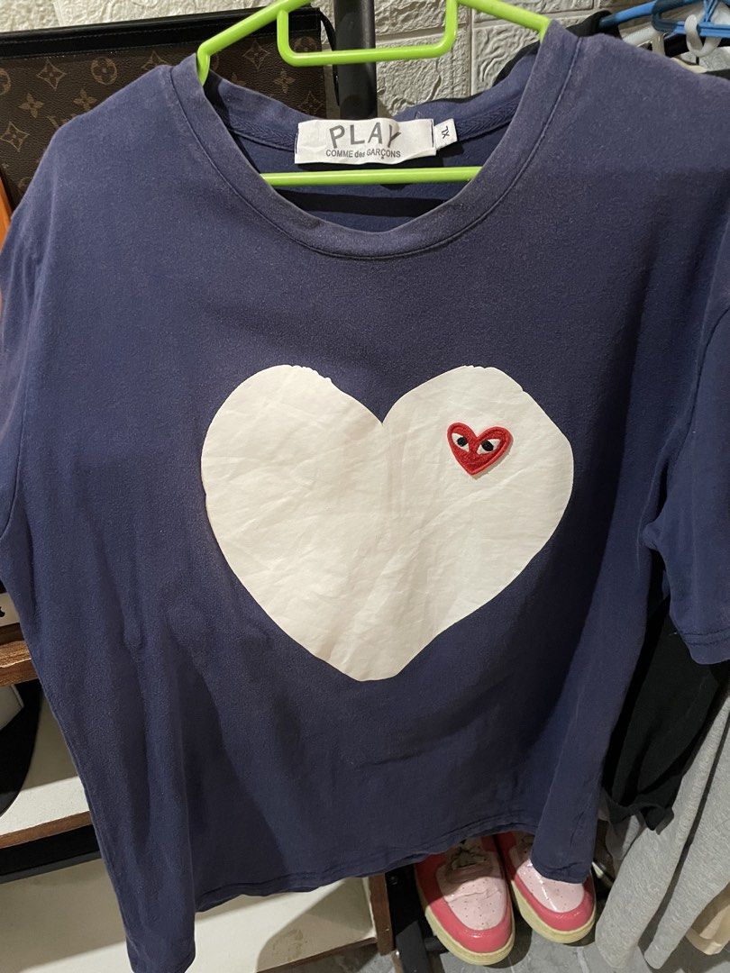 Comme des Garcons Play Heart T-shirt (Category: Shirts) located in San Fernando. Submitted by unc_thrifts (Listing ID 1432175799, Image 1). Description: - Comme des Garcons Play T-shirt - Color: Navy blue - Features a large white heart with red heart logo - Round neckline - Short sleeves - Size: XL - Material: Cotton.