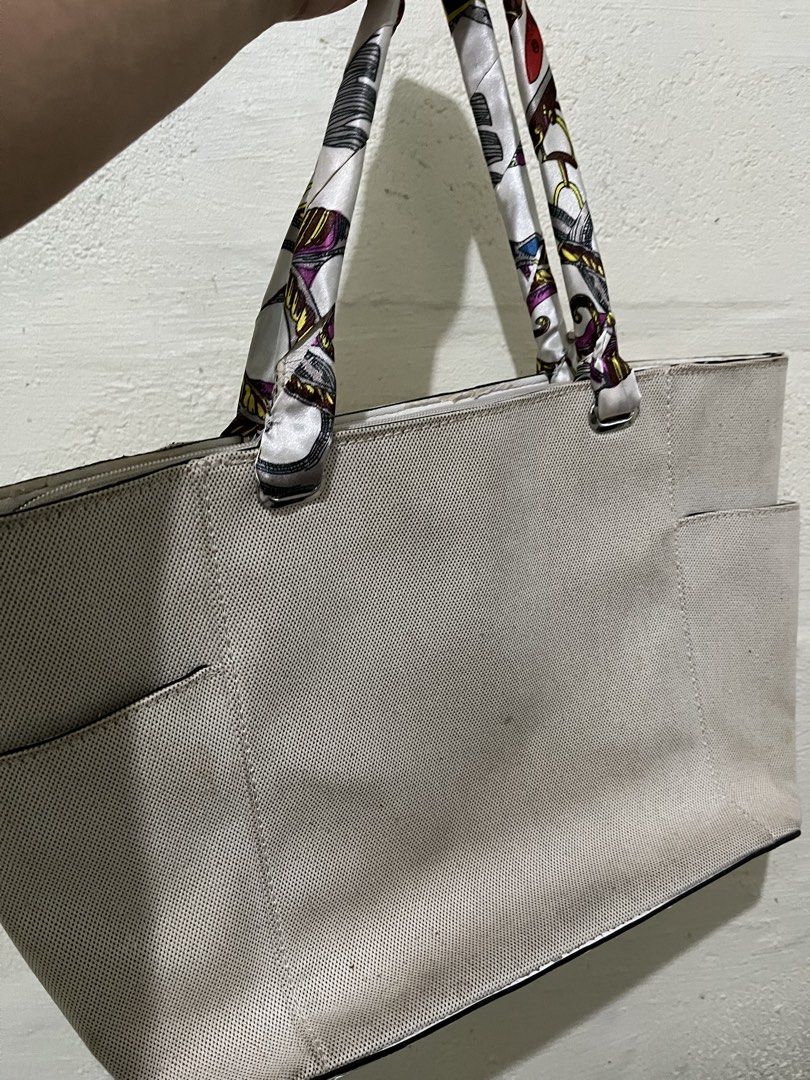 Guess Tote Bag with Scarf Handles (Category: Tote Bags) located in Mandaluyong City. Submitted by jane019 (Listing ID 1432147915, Image 3). Description: Guess tote bag features a beige canvas exterior with the brand name prominently displayed. It has a spacious interior with multiple pockets and a patterned lining. The bag includes decorative scarf handles. The bottom of the bag is white. It has side pockets and silver hardware. Can fit 14" lapto