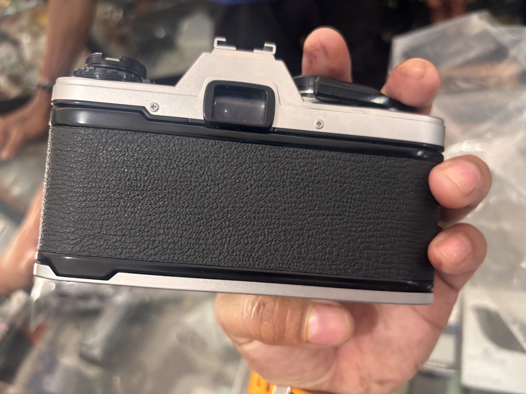 Olympus OM-10 Camera with Lens (Category: Cameras) located in Victoria. Submitted by eliphalez (Listing ID 1432066307, Image 3). Description: Olympus OM-10 camera with a 50mm lens. The camera body is silver and black. The lens has markings for various focal lengths and aperture settings. Includes a lens cap. The camera has a top dial for settings and a film advance lever. The back of the camera has a textured grip..