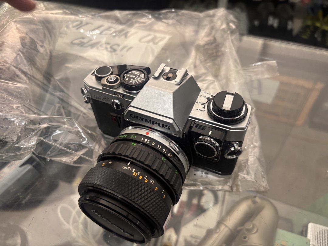 Olympus OM-10 Camera with Lens (Category: Cameras) located in Victoria. Submitted by eliphalez (Listing ID 1432066307, Image 1). Description: Olympus OM-10 camera with a 50mm lens. The camera body is silver and black. The lens has markings for various focal lengths and aperture settings. Includes a lens cap. The camera has a top dial for settings and a film advance lever. The back of the camera has a textured grip..