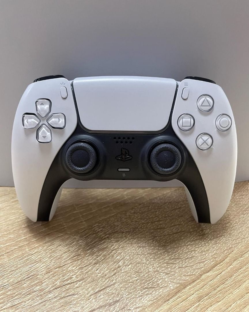 Sony PlayStation 5 Console (Category: PlayStation) located in Caloocan City. Submitted by truehawk.889b68 (Listing ID 1432027994, Image 3). Description: PlayStation 5 console is shown with a white and black design. It includes a white DualSense controller. The console is standing upright on a wooden surface. The controller is also placed on the wooden surface. The console has a sleek, modern aesthetic..