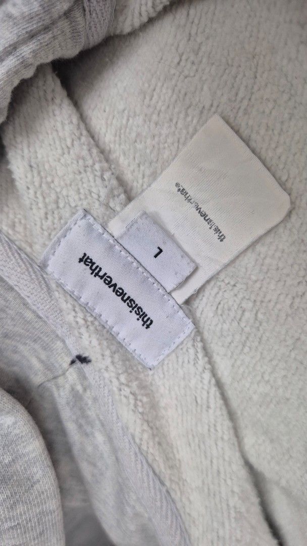 thisisneverthat Zip-Up Hoodie - Grey - Size L (Category: Hoodies) located in Valencia. Submitted by declutterainnn (Listing ID 1432002194, Image 2). Description: - thisisneverthat grey zip-up hoodie - Size: L - Features: Hood, front pockets, full-length zipper - Branding: Logo on front and back, brand name on zipper - Material: Soft, likely cotton blend.