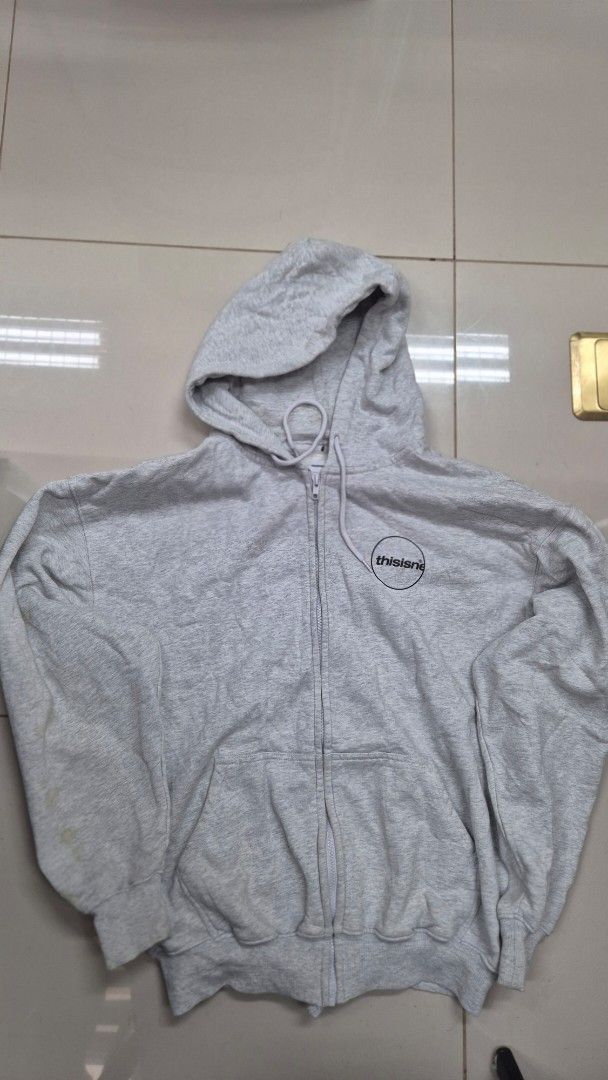 thisisneverthat Zip-Up Hoodie - Grey - Size L (Category: Hoodies) located in Valencia. Submitted by declutterainnn (Listing ID 1432002194, Image 1). Description: - thisisneverthat grey zip-up hoodie - Size: L - Features: Hood, front pockets, full-length zipper - Branding: Logo on front and back, brand name on zipper - Material: Soft, likely cotton blend.