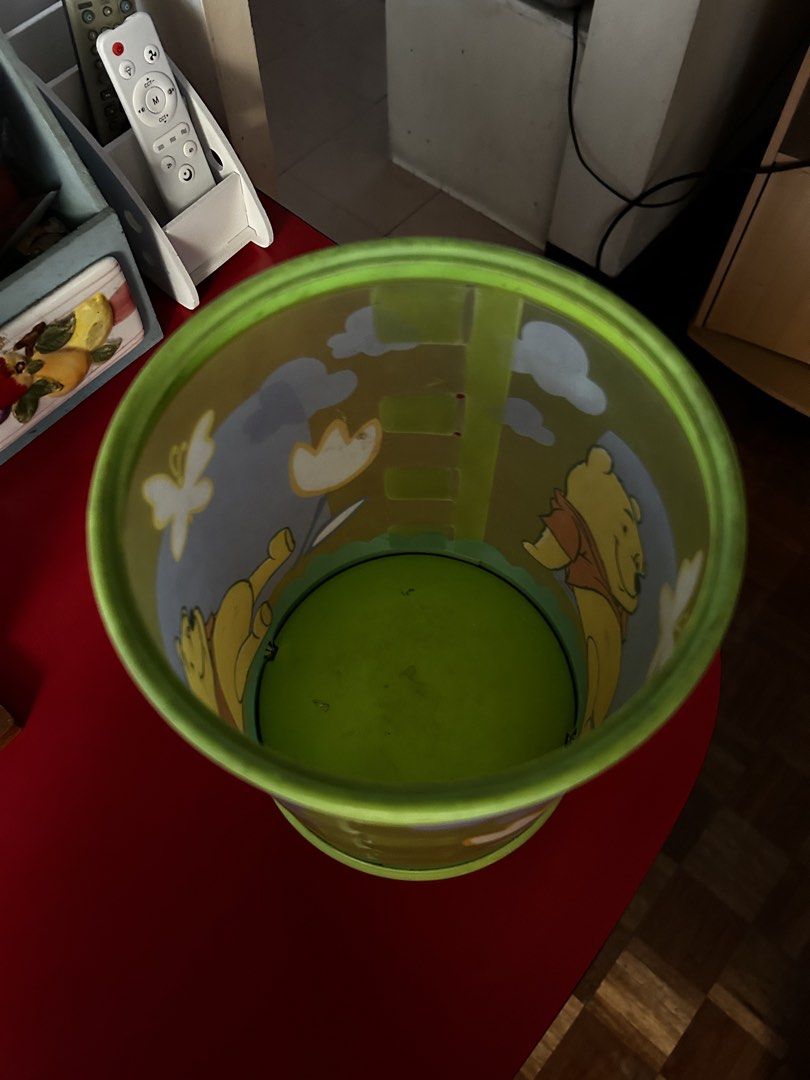 Disney Winnie the Pooh Storage Can (Category: Food Organization & Storage) located in Las Pinas. Submitted by rjmwings (Listing ID 1432255666, Image 2). Description: Winnie the Pooh-themed storage can. It features a green and yellow color scheme with illustrations of Winnie the Pooh, a butterfly, and clouds. It has a circular base and a cylindrical body. The bottom of the can has a design with the text "DESIGN PATENT APPLIED FOR". Can also be use