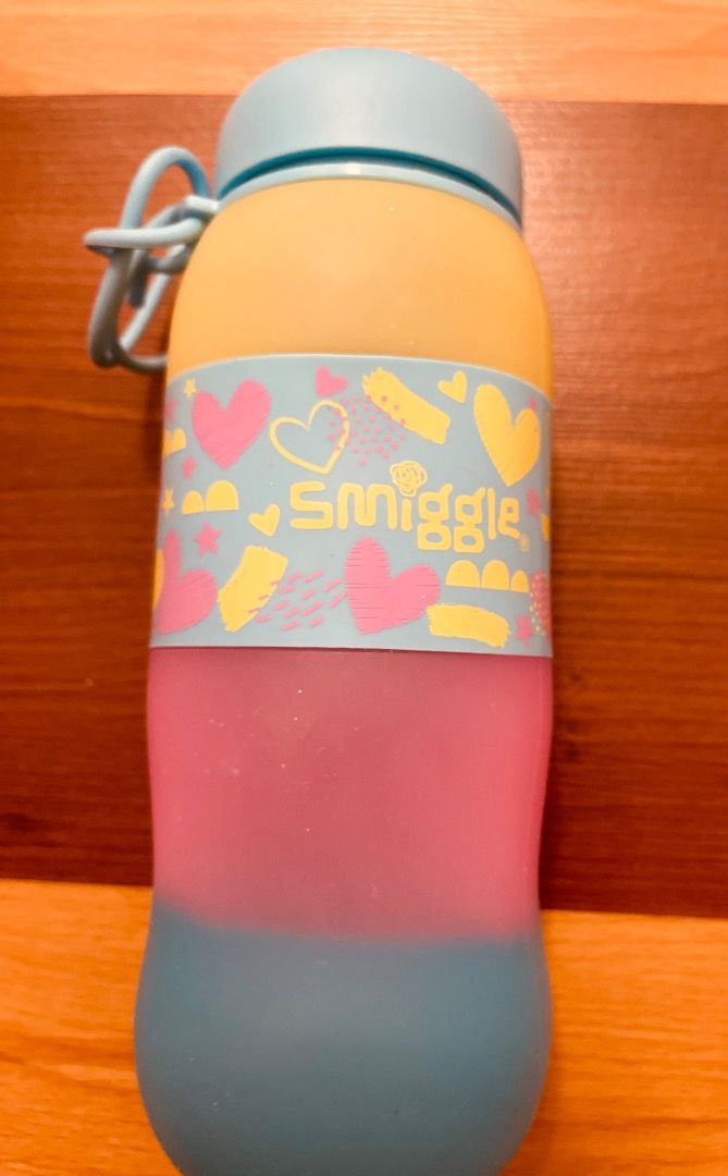 Smiggle Water Bottle (Category: Water Bottles & Tumblers) located in Pasig City. Submitted by royalregistry (Listing ID 1432314803, Image 3). Description: - Smiggle water bottle - Colorful design: yellow, pink, and blue sections - Includes a blue lid with a built-in straw - Comes with a matching blue carrying strap - Dimensions: Approximately 8 inches in height and 3 inches in width - Adorned with heart and star patterns.