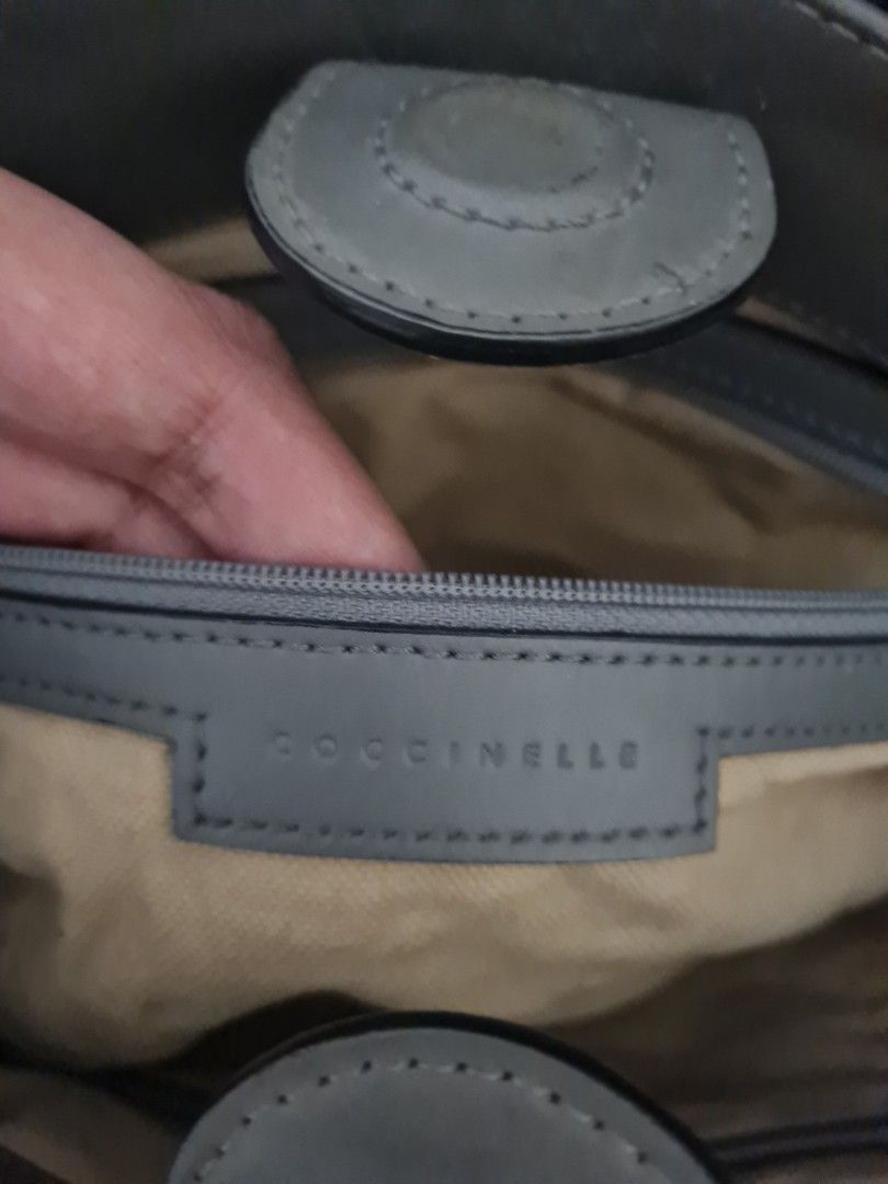 Coccinelle Grey Handbag (Category: Luxury Bags & Wallets) located in Quezon City. Submitted by thriftypieces (Listing ID 1432513469, Image 2). Description: - Grey Coccinelle 2 way bag (handbag and sling bag) but no sling - Top zipper closure - Dual top handles - Fabric lined interior with multiple compartments - Silver-tone hardware - Coccinelle logo on front, inside and cloth tag - Signs of wear: marks on exterior and strap, pen marks inside the
