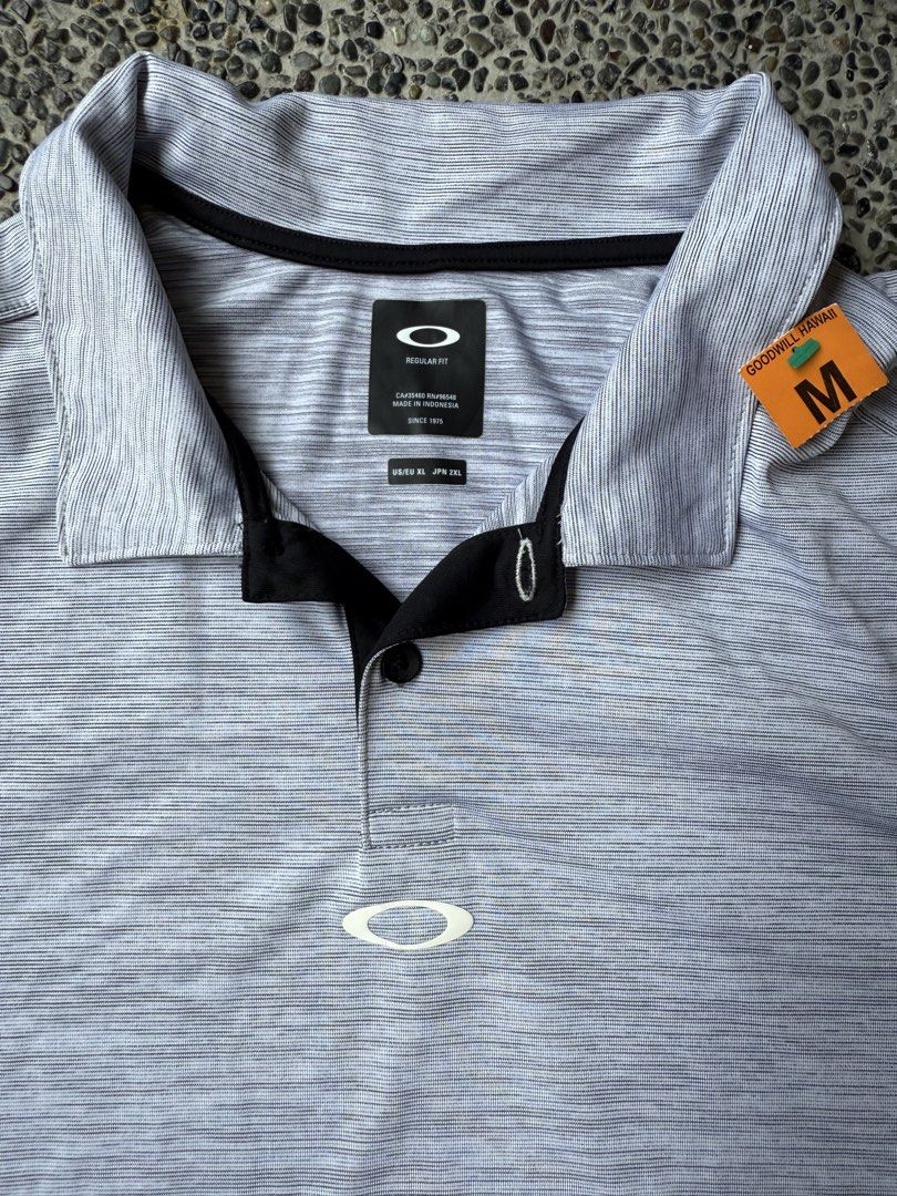Oakley Regular Fit Polo Shirt (Category: Tshirts & Polo Shirts ) located in Dinalupihan. Submitted by thrift.trips (Listing ID 1432564332, Image 2). Description: - Oakley polo shirt - Color: Gray - Size: M - Fit: Regular - Sleeves: Short - Collar: Collared with black accents - Features Oakley logo on chest and sleeve - Made in Indonesia - Length 31 - Width 23.5.
