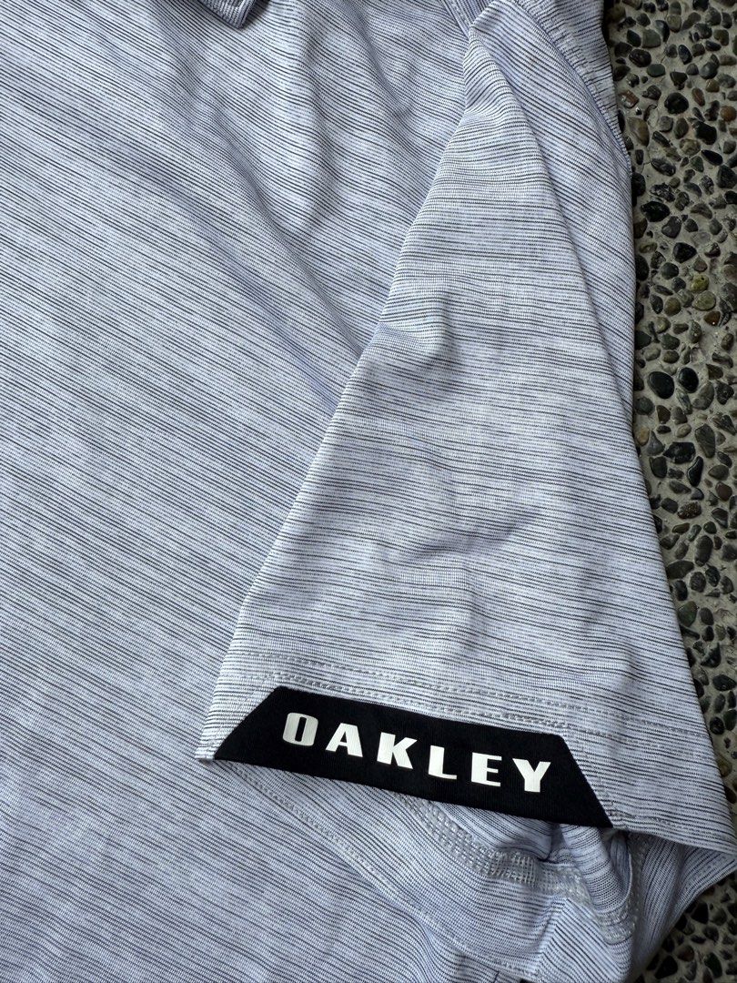 Oakley Regular Fit Polo Shirt (Category: Tshirts & Polo Shirts ) located in Dinalupihan. Submitted by thrift.trips (Listing ID 1432564332, Image 3). Description: - Oakley polo shirt - Color: Gray - Size: M - Fit: Regular - Sleeves: Short - Collar: Collared with black accents - Features Oakley logo on chest and sleeve - Made in Indonesia - Length 31 - Width 23.5.
