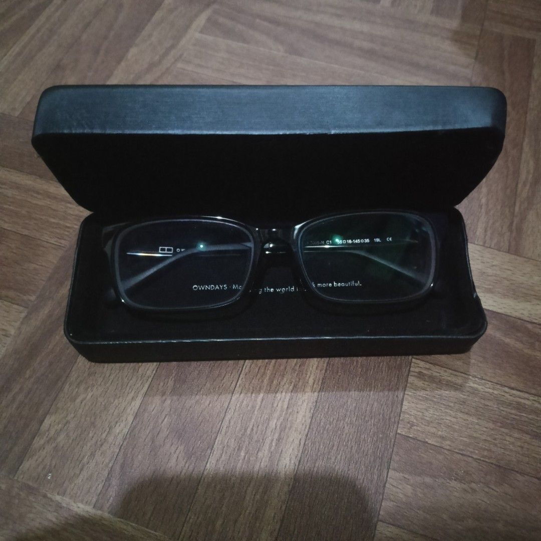 Owndays (Category: Sunglasses & Eyewear) located in Cabanatuan. Submitted by flipmopickmo (Listing ID 1432401555, Image 3). Description: A sleek pair of OWNDAYS eyeglasses is presented in a minimalist black case, set against a warm wooden floor. The rectangular frames feature a clean, modern silhouette with slightly rounded edges, offering a refined yet everyday look. Close-up details reveal the inner temple markings, including the model code 200