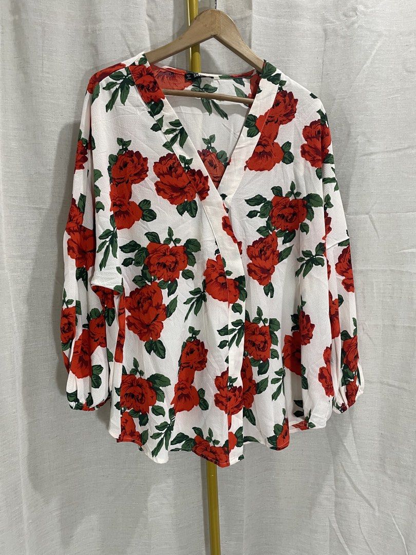 SHEIN Floral Wrap Blouse 2XL (Category: Blouses) located in Quezon City. Submitted by 27ValiantStreet_Storefront (Listing ID 1432499177, Image 1). Description: - SHEIN floral wrap blouse - Size: 2XL - Design: Red rose print on white background - Features: Long sleeves, wrap design with tie closure - Origin: Made in China.