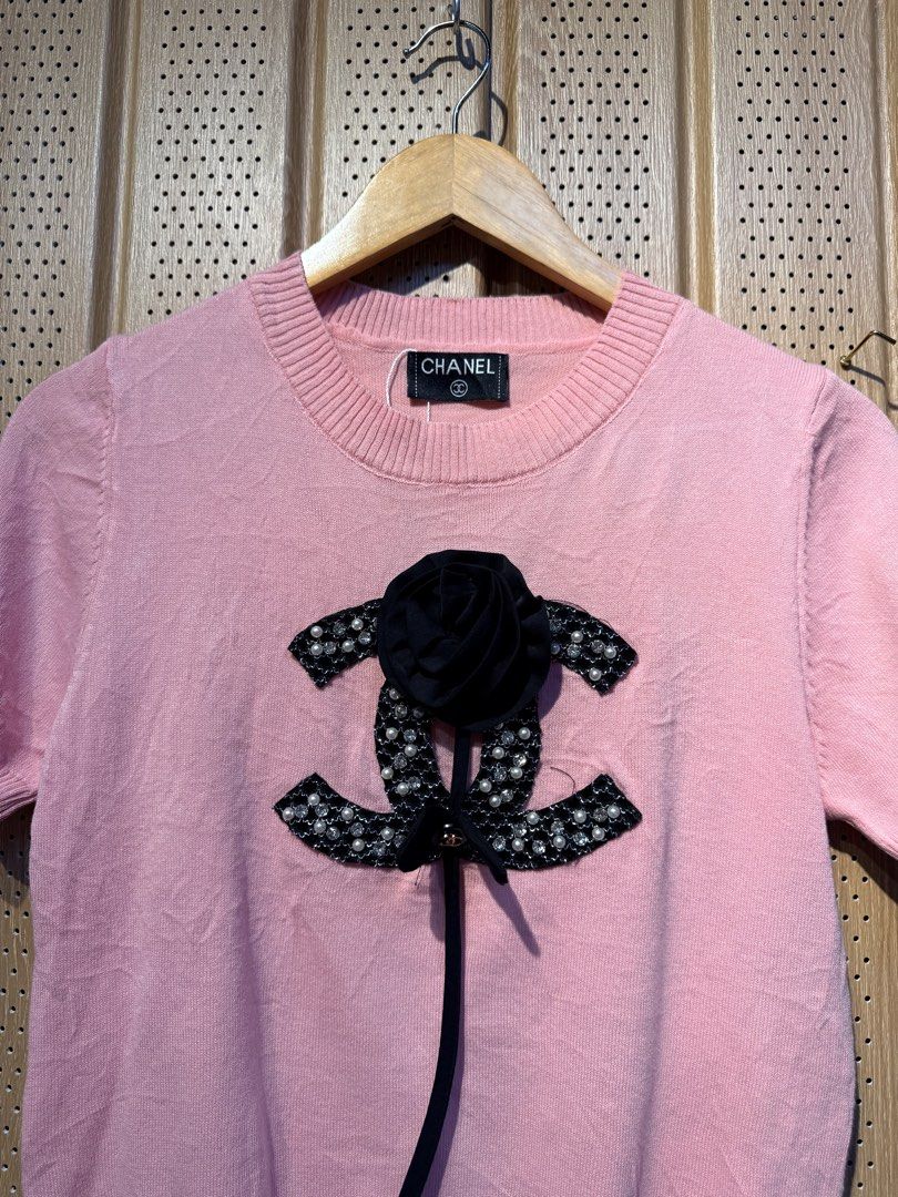 Chanel Pink Short Sleeve Top (Category: Shirts) located in Santiago. Submitted by twicebutnice03 (Listing ID 1432613458, Image 2). Description: - Authentic Chanel top - Lovely pink color - Short sleeves - Round neckline - Features a decorative Chanel logo with black flower and ribbon detail - Made of knit material - Chanel label visible Size & Dimes:MEDIUM-LARGE 19”22.