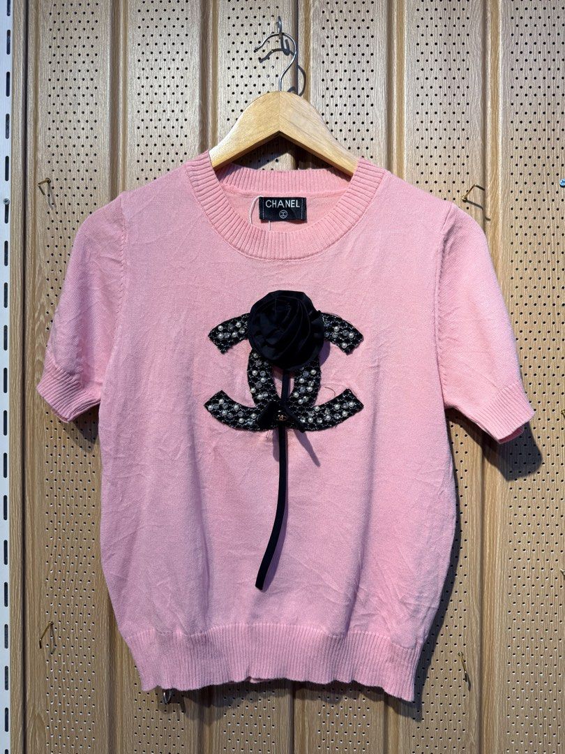 Chanel Pink Short Sleeve Top (Category: Shirts) located in Santiago. Submitted by twicebutnice03 (Listing ID 1432613458, Image 3). Description: - Authentic Chanel top - Lovely pink color - Short sleeves - Round neckline - Features a decorative Chanel logo with black flower and ribbon detail - Made of knit material - Chanel label visible Size & Dimes:MEDIUM-LARGE 19”22.