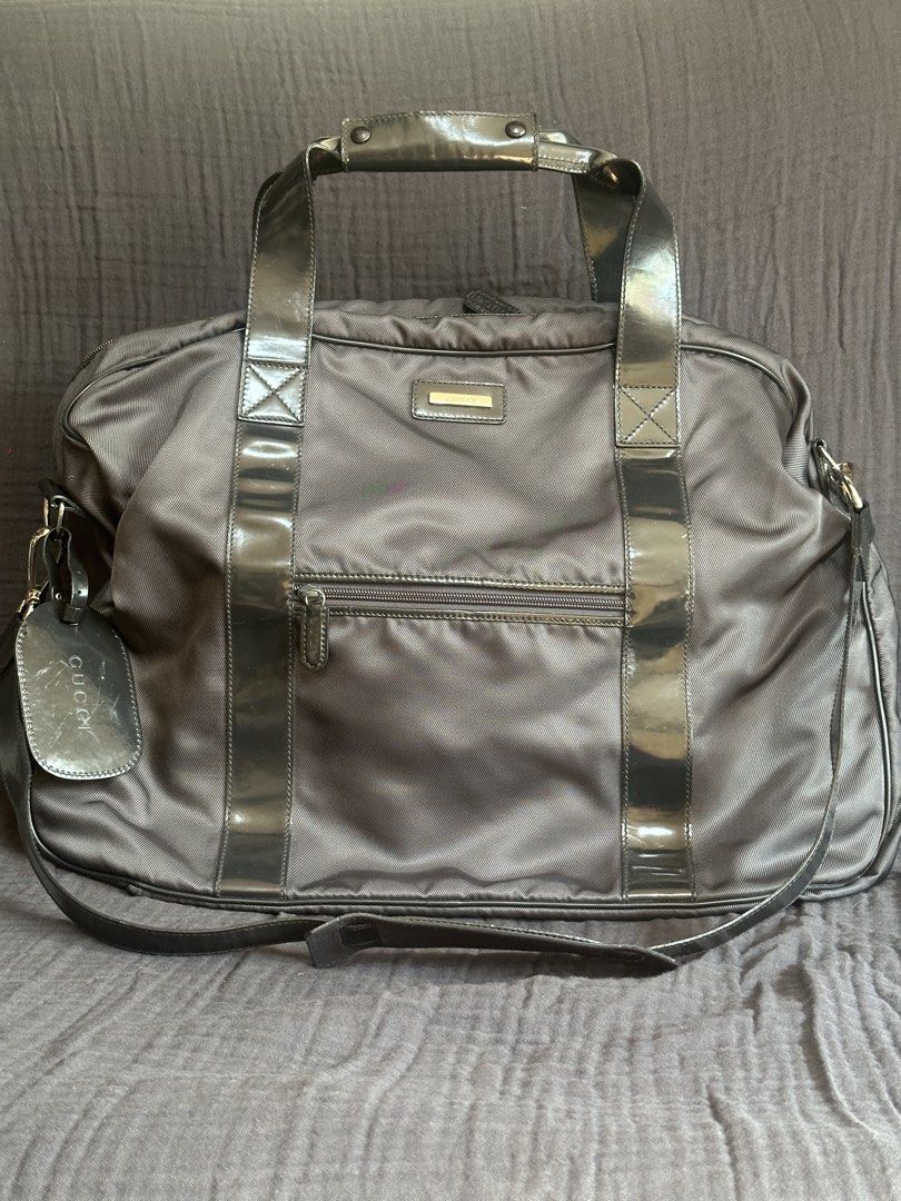 Gucci Travel Bag (Category: Luxury Bags & Wallets) located in Mandaluyong City. Submitted by marceditems (Listing ID 1432698136, Image 1). Description: Gucci travel bag made of gray nylon and metallica gray leather with a top handle and a detachable shoulder strap. It has a front zip pocket and multiple zippers with the Gucci logo. The interior includes straps for securing items. The bag has a luggage tag with the Gucci logo and serial number. Ma